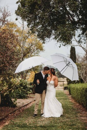 Gledswood Wedding - Groom stand kissing his bride under white umbrellas as it rains on their wedding day