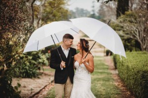 Gledswood Wedding - A bride and groom stand under white umbrellas as it rains on their wedding day