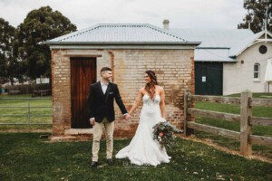 Gledswood Wedding - A bride and groom hold hands against a small brick building at their Gledswood Wedding