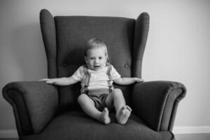 Baby boy sitting in a large armchair in a studio, black and white image