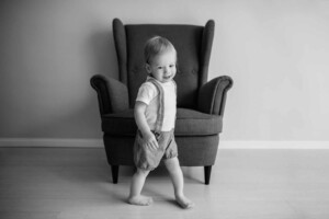 Baby boy standing in front of an armchair, black and white photograph