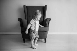 A little boy stands steadying himself against an armchair