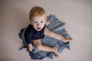 Baby boy gazes up at the camera, sitting on a blue felt matt