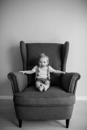 Baby boy sitting in a large armchair in a studio, black and white image
