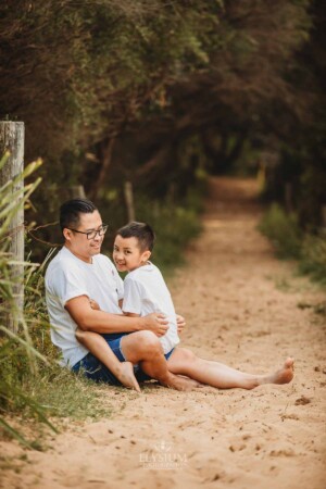 A father sits cuddling his son on a sandy beach path