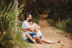 A father sits cuddling his son on a sandy beach path