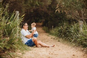A father sits cuddling his son on a sandy beach path
