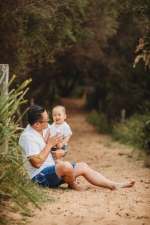 A father sits cuddling his son on a sandy beach path