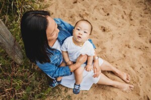 A mother sits cuddling her son on a sandy beach path