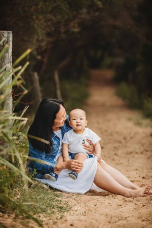 A mother sits cuddling her son on a sandy beach path