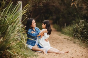 A mother sits cuddling her daughter on a sandy beach path
