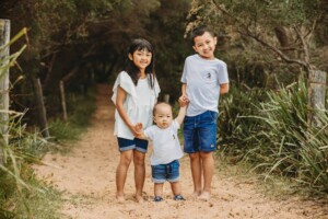 3 children stand holding hands on a sandy beach path