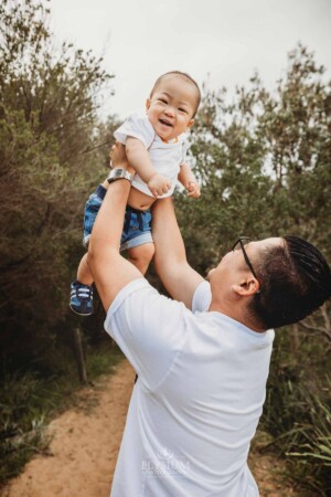 A dad lifts his little boy above him in the bush
