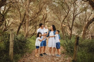 A family cuddle together while standing on a bushy beach path