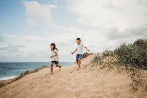 2 children race down a sand dune at sunset
