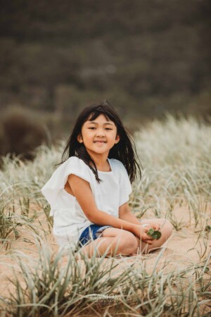 A little girl sits on a grassy sand dune at sunset
