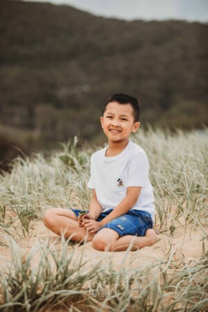 A little boy sits on a grassy sand dune at sunset
