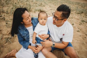 Parents cuddle their baby boy sitting on a beach