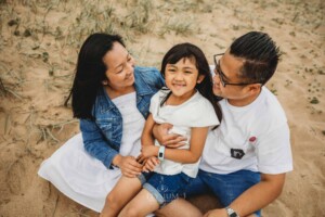 Parents sit on a sand dune and cuddle their daughter