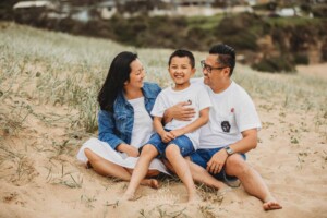 Parents sit on a sand dune and cuddle their son