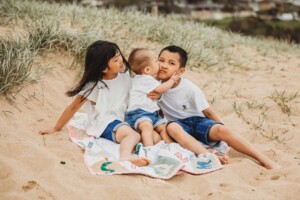3 children sit on a rug at the beach