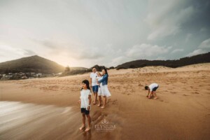 A family stand on a beach with the sun setting behind them