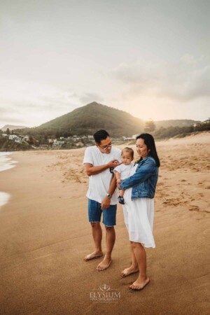 Parents cuddle their baby boy on a beach at sunset