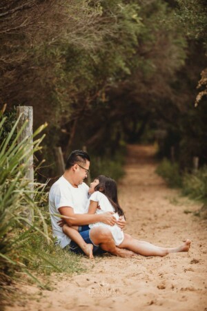 A father sits cuddling his daughter on a sandy beach path