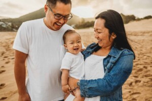 Parents cuddle their baby boy on a beach at sunset