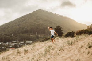 A little boy races down a beach sand dune at sunset