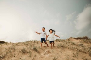 2 children hold hands as they run down sand dunes