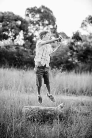 A boy jumping off a log in a grass field at sunset