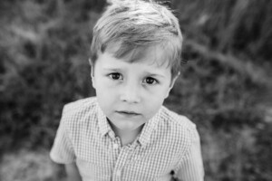 Black & white portrait of a little boy standing in a grassy field