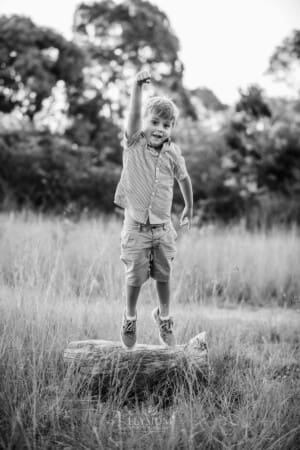 A boy jumping off a log in a grass field at sunset