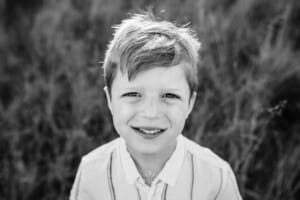 Black & white portrait of a little boy standing in a grassy field