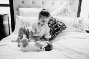 Newborn session - a boy sits on his parents bed with his baby sister