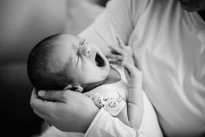 Newborn session - A baby girl yawns as she is held by her mother