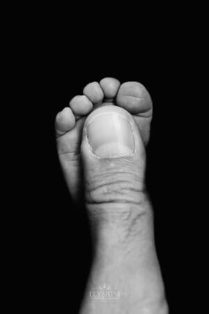 Newborn session - A father's thumb showing how tiny his baby's foot is