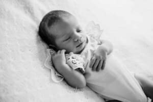 Newborn session - A baby sleeping on her back laying on a white blanket
