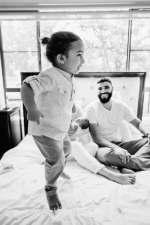 Newborn session - A little boy jumps on his parents bed as they watch