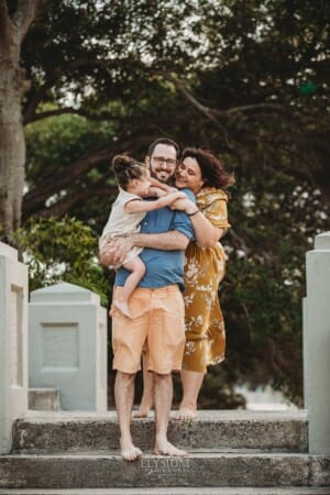 Family Photographer - Parents hug their little girl on steps at Balmoral beach