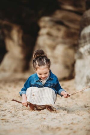 Family Photographer - A little girl digs in the sand with sticks at Balmoral beach