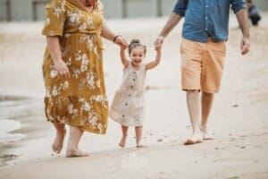 Family Photographer - Parents swinging their little girl as she walks between them at the beach