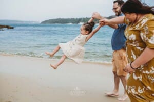 Family Photographer - Parents swinging their little girl as she walks between them at the beach