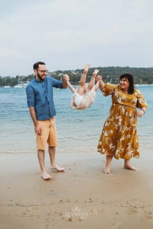 Family Photographer - Parents swinging their little girl as she walks between them at the beach