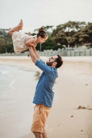 Family Photographer - A dad lifts his little girl in the air standing on the beach