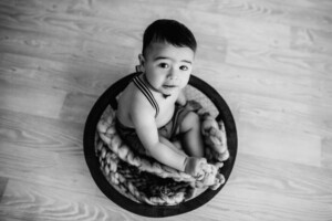 Baby boy sitting in a wooden bowl, black and white image shot from above