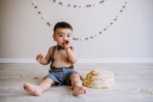 A little boy sucks icing off his fingers after a cake smash session