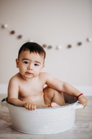 A baby boy sits in a white tub to clean up his cake smash