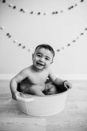 Baby boy bathing after his cake smash in a white vintage tub